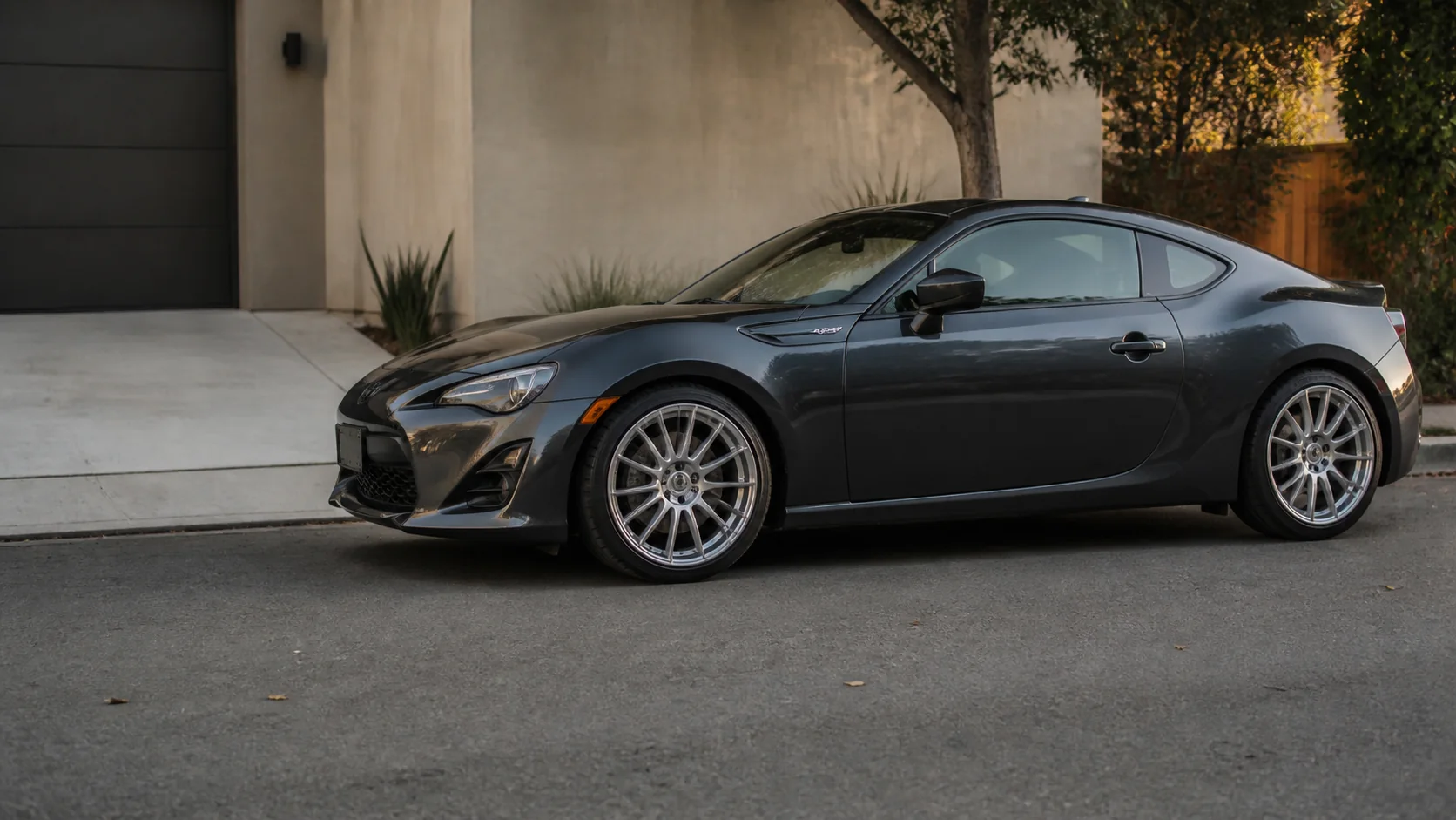 Graphite coupe with brushed silver wheels parked in a real residential driveway